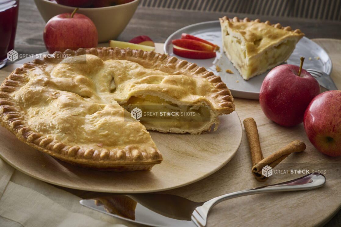 Apple Pie With a Slice Taken Out, Surrounded by Whole Fresh Apples on a Wooden Table Surface