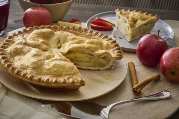 Apple Pie With a Slice Taken Out, Surrounded by Whole Fresh Apples on a Wooden Table Surface