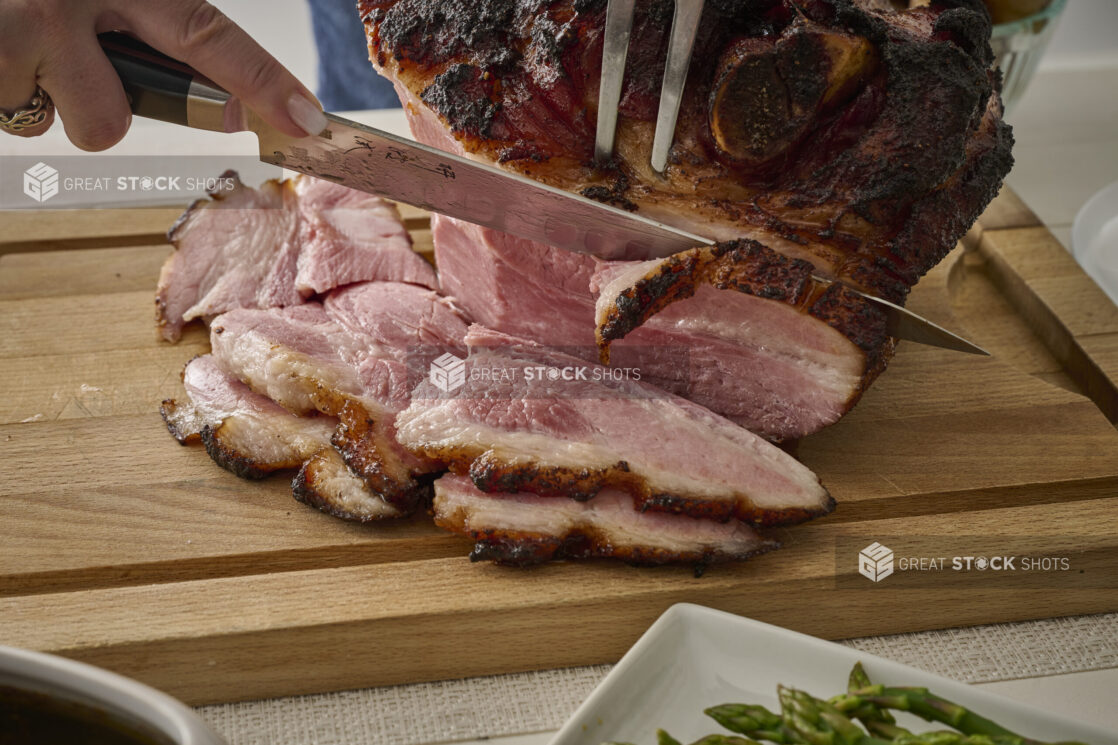 Close Up of Hands Carving an Easter Ham on a Wooden Cutting Board in an Indoor Setting