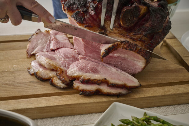 Close Up of Hands Carving an Easter Ham on a Wooden Cutting Board in an Indoor Setting
