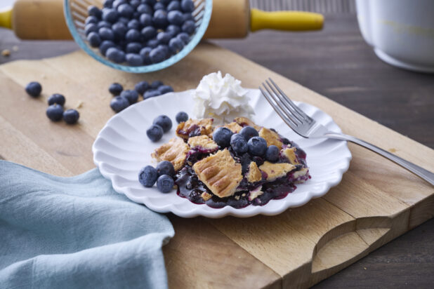 Blueberry Pie Crumble Dessert with Fresh Whipped Cream and Blueberries on a White Ceramic Plate on a Wooden Cutting Board