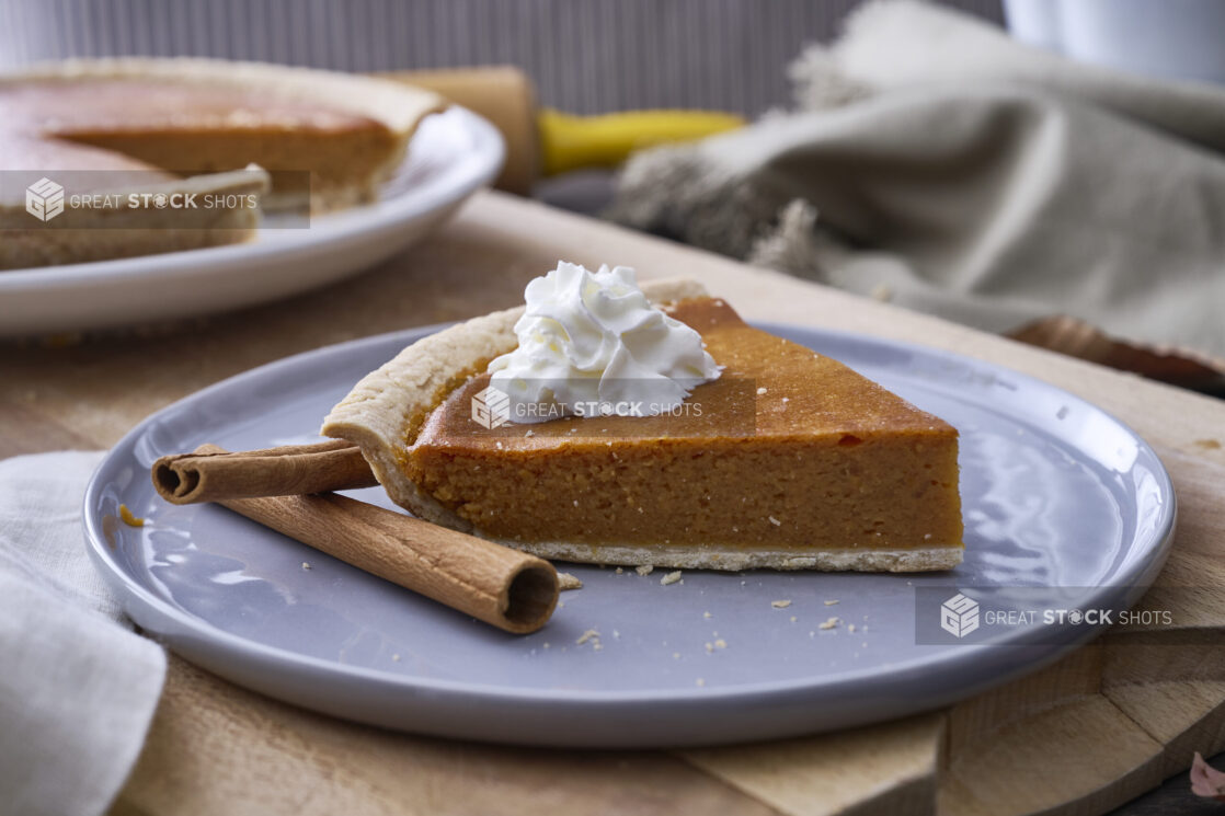 Close Up of a Slice of Pumpkin Pie with Whipped Cream Garnish and Cinnamon Sticks on a Grey Ceramic Dish