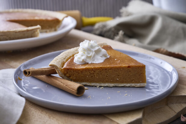Close Up of a Slice of Pumpkin Pie with Whipped Cream Garnish and Cinnamon Sticks on a Grey Ceramic Dish