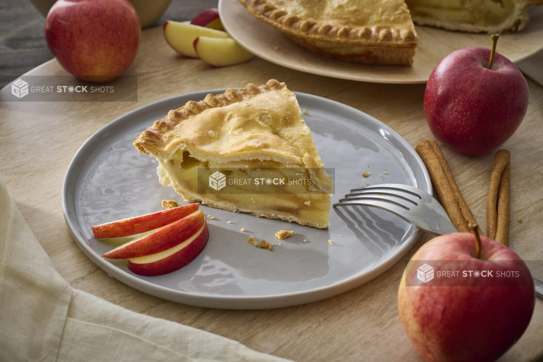 Slice of Apple Pie with Fresh Apple Slices on a Grey Ceramic Dish Surrounded by Fresh Whole Apples in an Indoor Setting - Variation