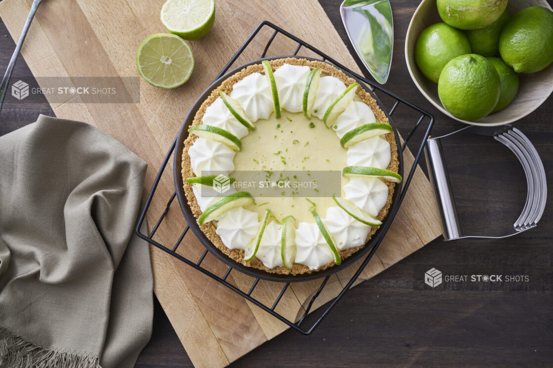 Overhead View of a Whole Key Lime Pie with Sliced Lime and Whipped Cream Garnish on a Cooling Rack in an Indoor Setting