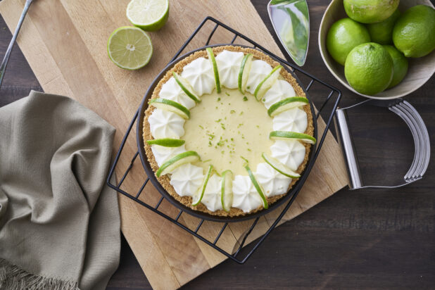 Overhead View of a Whole Key Lime Pie with Sliced Lime and Whipped Cream Garnish on a Cooling Rack in an Indoor Setting