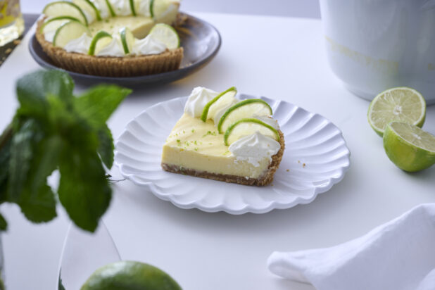 Slice of Key Lime Pie with Whipped Cream and Lime Slice Garnish on a Decorative White Plate on a White Table Surface in an Indoor Setting - Variation