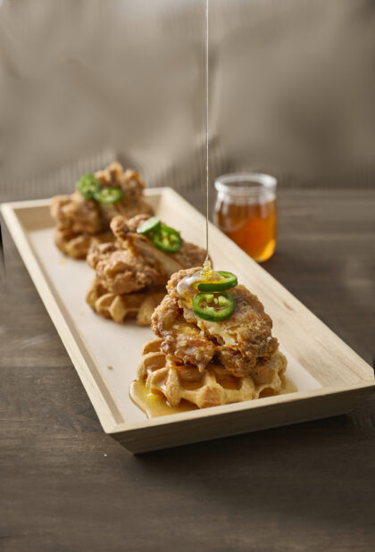 Trio of Fried Chicken and Waffles with Jalapeño Pepper Garnish and Honey Drizzle on a Narrow Rectangular Wood Catering Tray