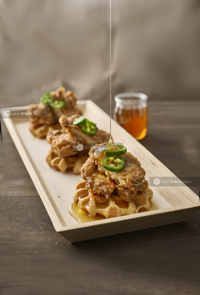 Trio of Fried Chicken and Waffles with Jalapeño Pepper Garnish and Honey Drizzle on a Narrow Rectangular Wood Catering Tray