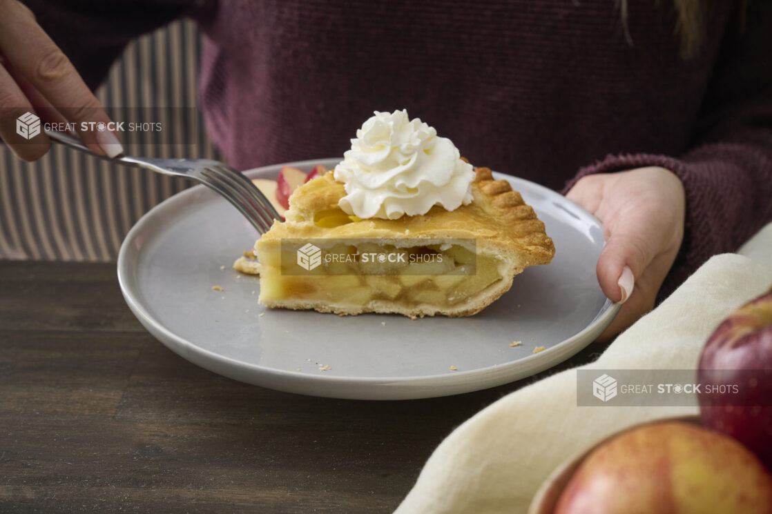 Person Eating a Apple Pie with Whipped Cream Garnish on a Grey Ceramic Dish in an Indoor Setting