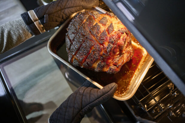 Overhead View of Hands Pulling a Roasted Ham Out of a Kitchen Oven in an Indoor Home Setting