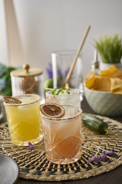 Citrus Margaritas with Dried Fruit Garnish in Glass Tumblers on a Woven Placemat in an Indoor Setting – Variation 2