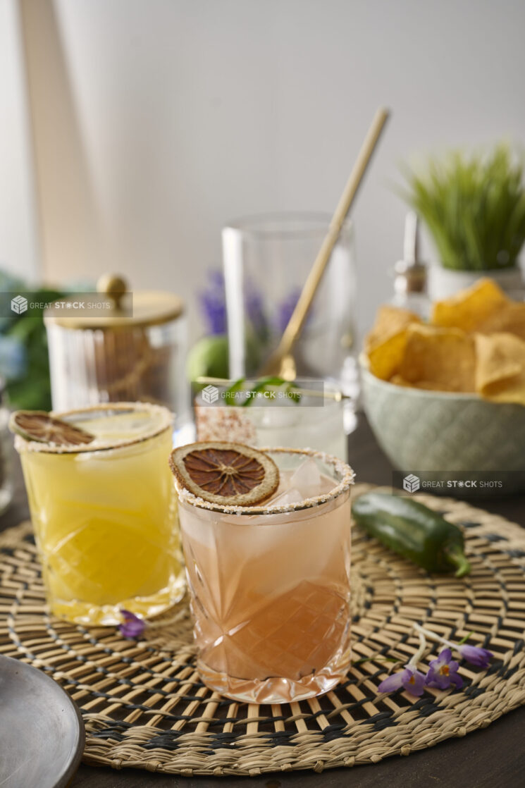 Citrus Margaritas with Dried Fruit Garnish in Glass Tumblers on a Woven Placemat in an Indoor Setting – Variation 2