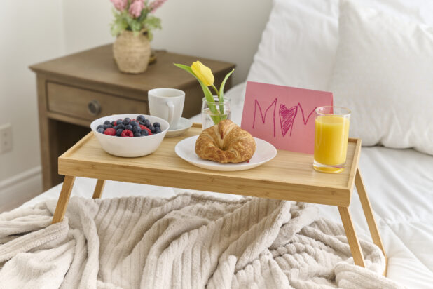 Breakfast in Bed From a Child to Their Mother with Croissant and Berries on a Bamboo Tray Table in a Bedroom Setting