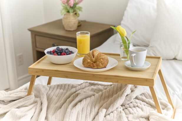 Breakfast in Bed with Croissant, a Bowl of Berries, Coffee and Juice on a Bamboo Tray Table in a Bedroom Setting
