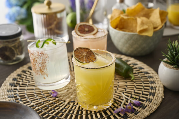 Orange Margarita with a Dried Lime Wheel and Other Assorted Margaritas in Glass Tumblers on a Woven Placemat in an Indoor Setting - Variation