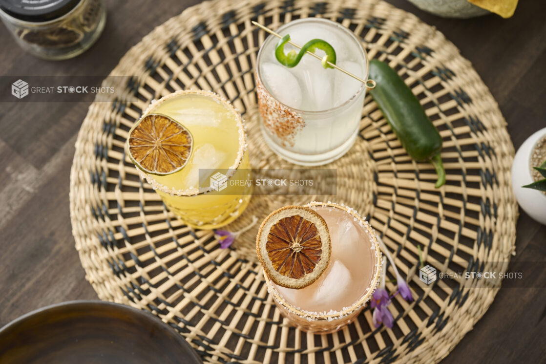 Overhead View of Citrus Margaritas with Dried Fruit Garnish in Glass Tumblers on a Woven Placemat in an Indoor Setting