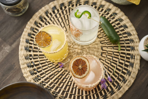 Overhead View of Citrus Margaritas with Dried Fruit Garnish in Glass Tumblers on a Woven Placemat in an Indoor Setting