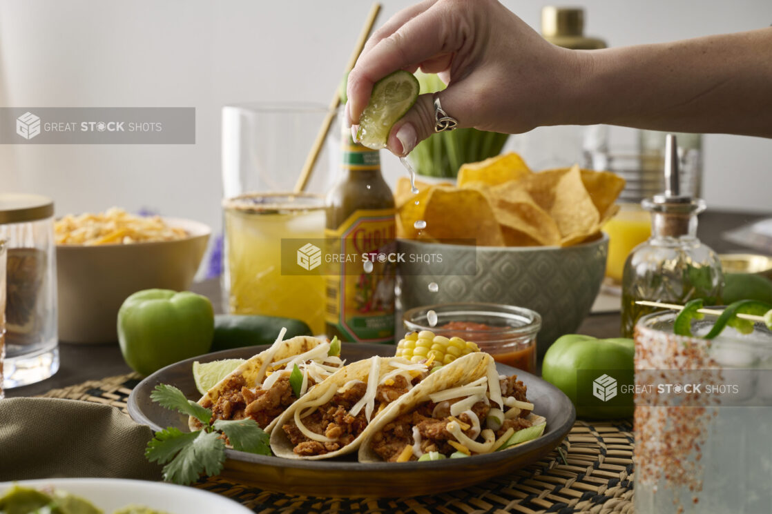 A Woman’s Hand Squeezes a Fresh Lime Wedge Over a Trio of Soft Tacos in a Dark Brown Dish in an Indoor Setting – Sequence 4