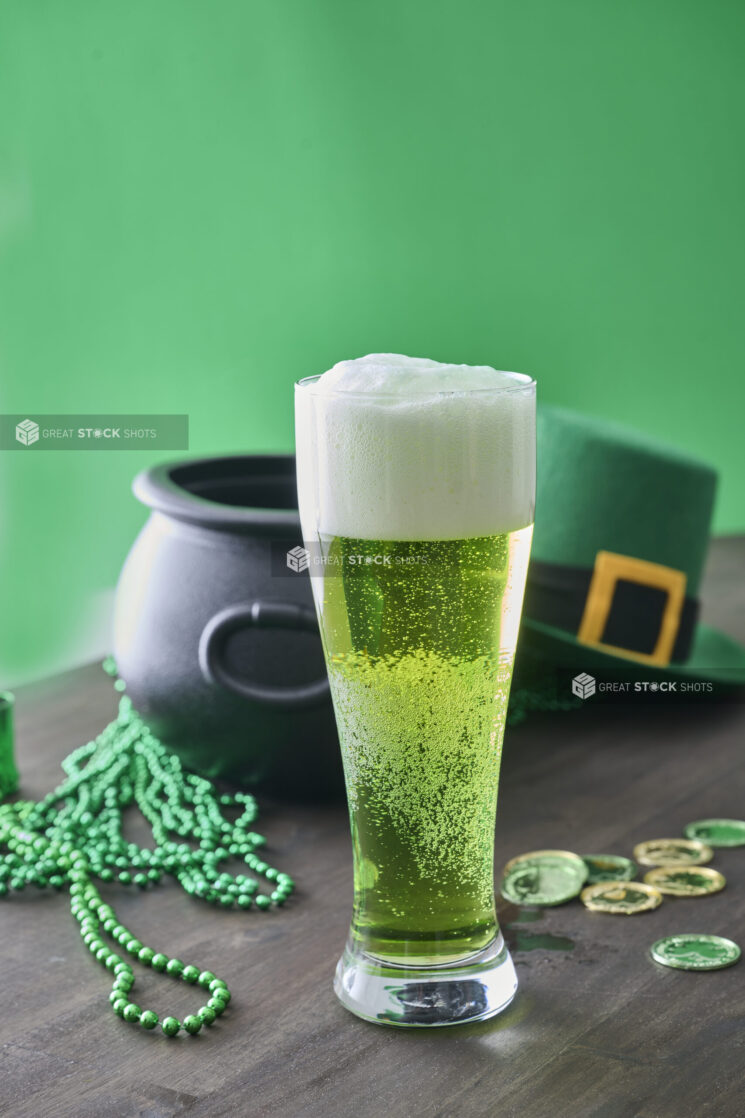 A Pint of Green Beer Surrounded by St. Patrick's Day Decorations on a Dark Wood Table in an Indoor Setting