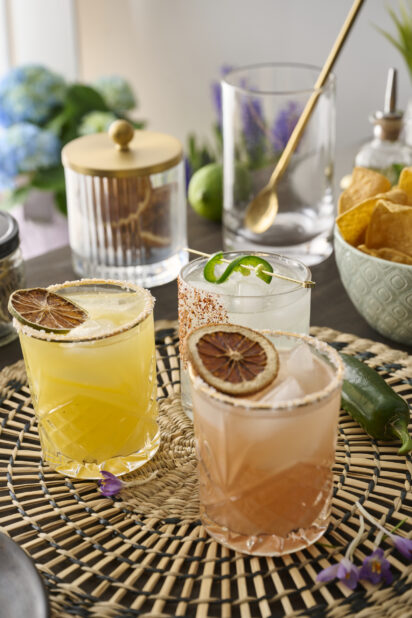 Citrus Margaritas with Dried Fruit Garnish in Glass Tumblers on a Woven Placemat in an Indoor Setting