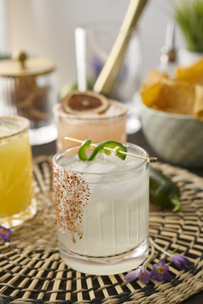 Margarita with Tajin Spice Rim and Jalapeño Pepper Garnish on a Woven Placemat in an Indoor Setting - Sequence 1
